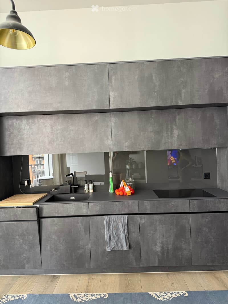 Modern kitchen with grey cabinets, a large sink, and a wooden cutting board on the counter.