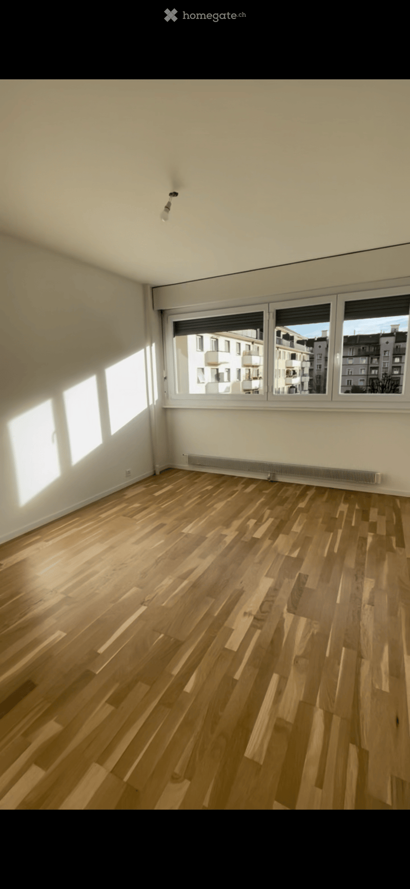 Empty room with wooden flooring, white walls, large windows, and a radiator. No furniture or equipment present.