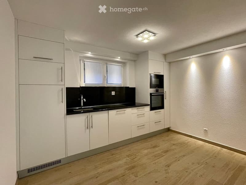 Modern kitchen with white cabinets, black countertop, stainless steel appliances, and wooden flooring.