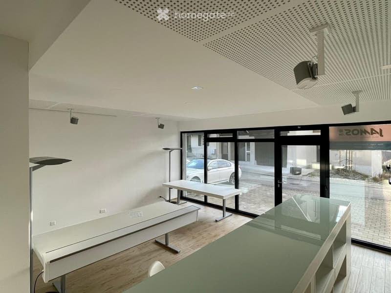 Modern, open-plan room with white tables, chairs, a glass reception desk, large windows, and a sleek design.