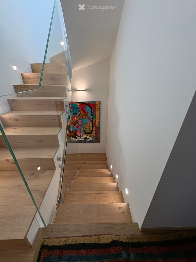 Modern wooden staircase with glass railing, integrated LED lighting, and a colorful abstract painting on the wall.