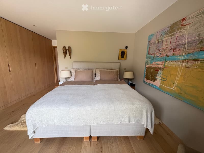 Modern bedroom with a large bed, nightstands, lamps, and a large abstract painting on the wall. Wooden flooring and built-in wardrobe.