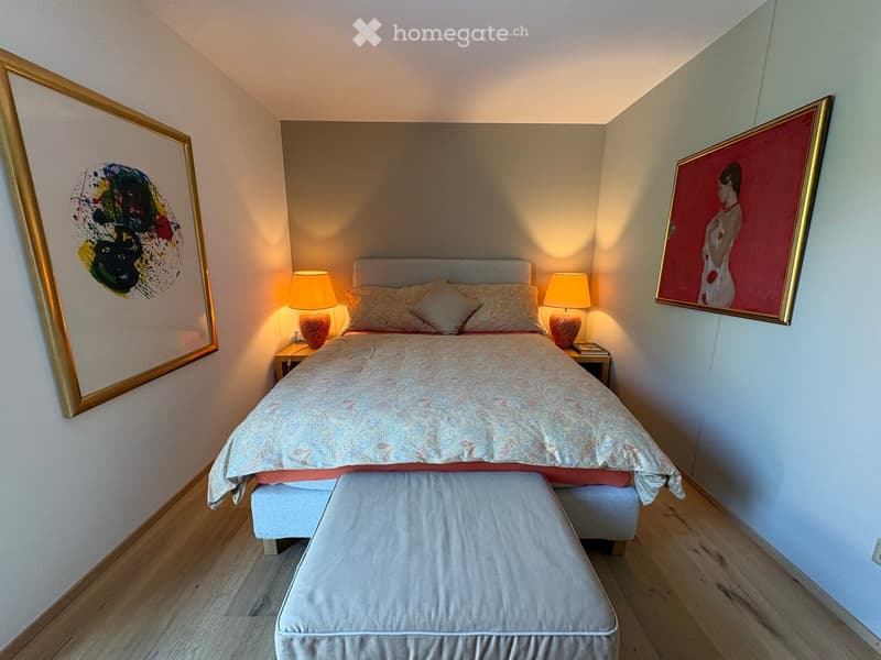 Cozy bedroom with a large bed, two nightstands with table lamps, a bench at the foot of the bed, and two framed paintings on the walls.