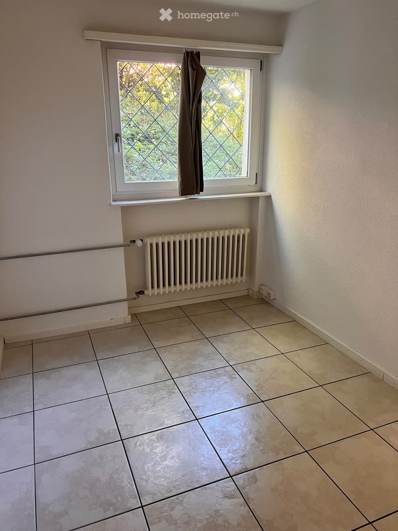 Empty room with tiled floor, white radiator, window with diamond-patterned glass and curtain, and light-colored walls.