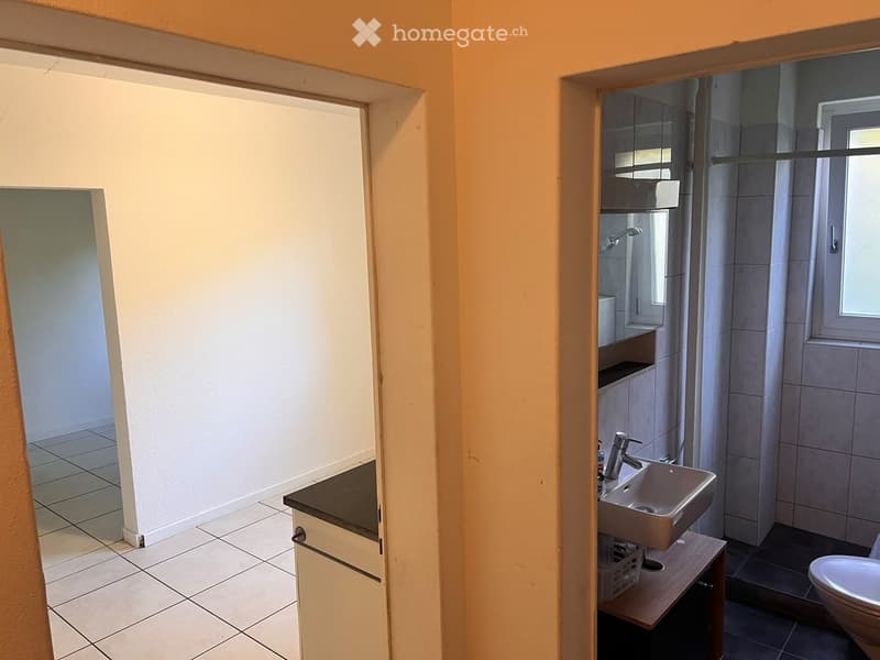 Bathroom with a sink, faucet, cabinet, and toilet. The space features tiled floors and walls, with a window providing natural light.