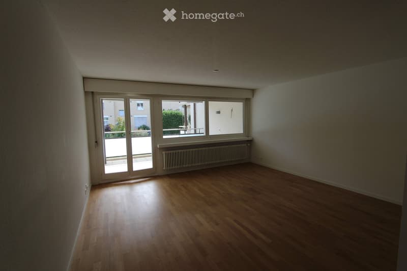 Empty room with wooden flooring, white walls, large windows, and a radiator under one window.