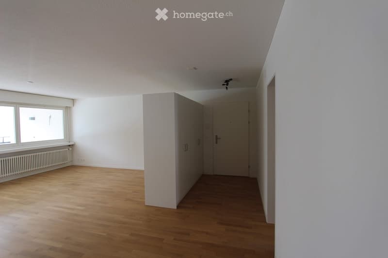 Empty room with wooden flooring, white walls, a window with a radiator below, and a door leading to another space.