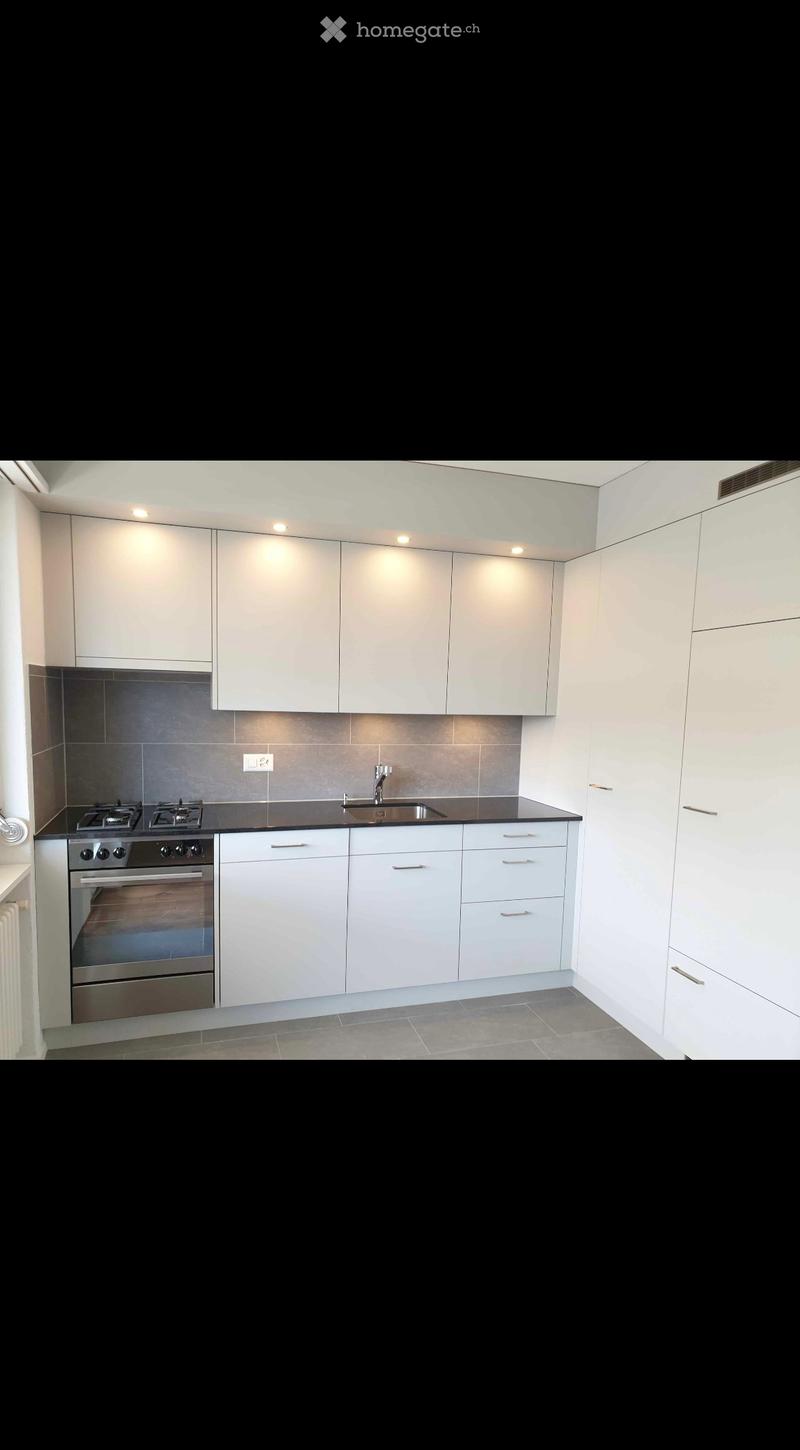 Modern kitchen with white cabinets, stainless steel oven, sink, and faucet, featuring a black countertop and gray tiled floor.