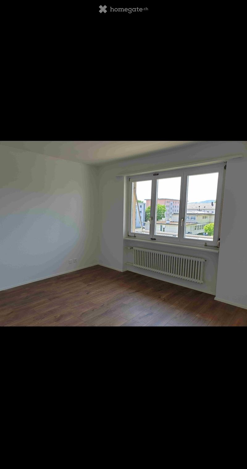 Empty room with wooden flooring, white walls, and large windows offering a view of the cityscape.