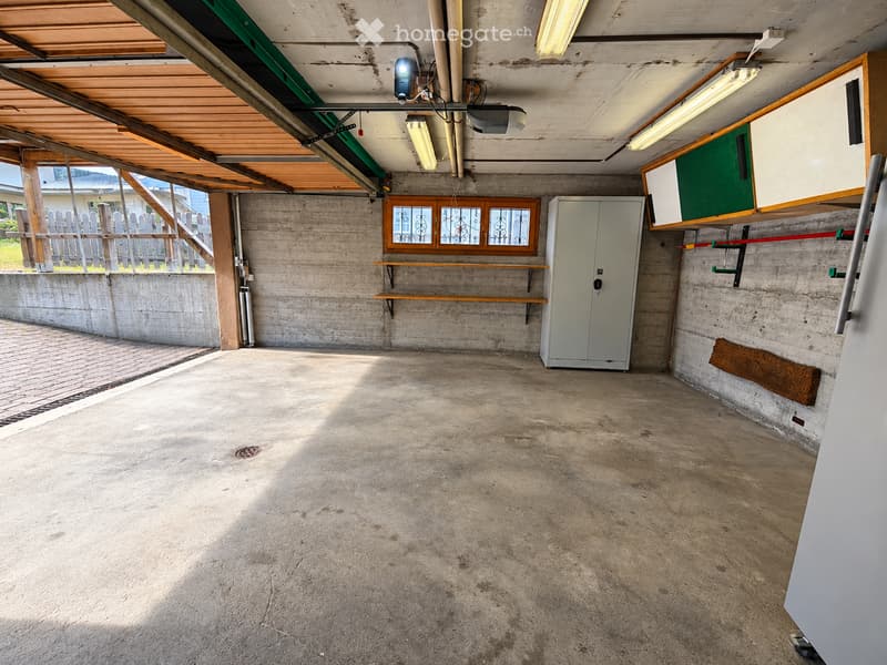 Empty garage with concrete floor, wooden ceiling, shelves, and a window with decorative glass panes.