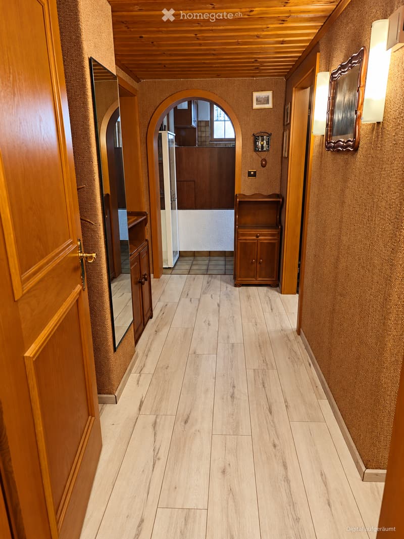 Wooden hallway with light-colored wooden flooring, wooden ceiling, and textured walls. Features arched doorways leading to other rooms, small wooden cabinets, and wall-mounted lighting fixtures.
