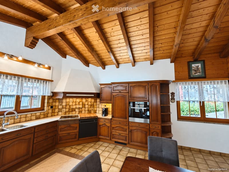 Cozy kitchen with wooden cabinets, stainless steel appliances, and a sink area. Features exposed wooden beams on the ceiling and large windows with sheer curtains.