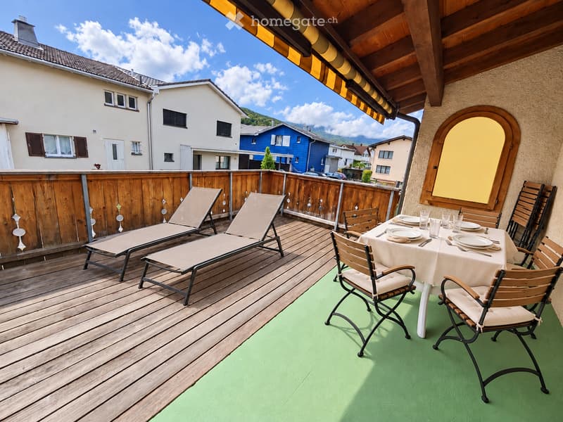 Balcony with wooden decking, green flooring, lounge chairs, dining table with chairs, and a view of neighboring houses.