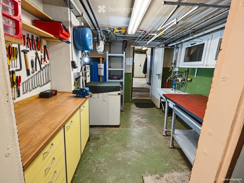 Workshop with wooden counter, tools on wall, shelves, sink, worktable, and cabinets.