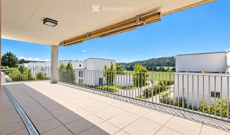 Balcony with tiled floor, metal railing, and a view of a green landscape and modern buildings.