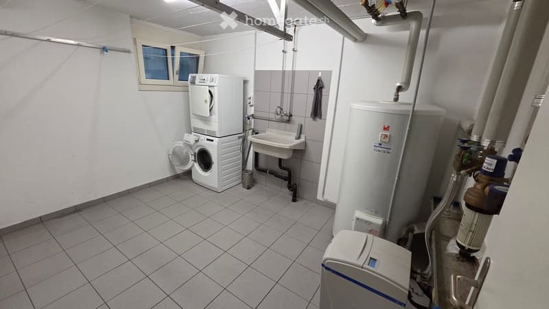 Utility room with a washing machine, sink, water heater, and various pipes and valves.