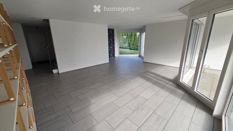 Empty room with grey tiled floor, white walls, large windows, and a staircase leading to another level.