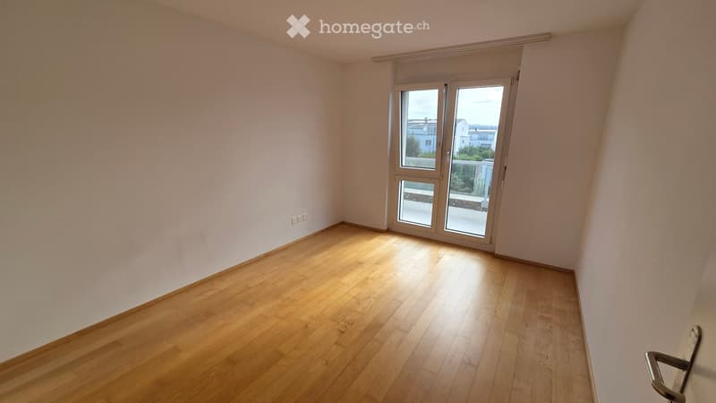Empty room with light wooden flooring and white walls, featuring a large sliding glass door leading to a balcony.