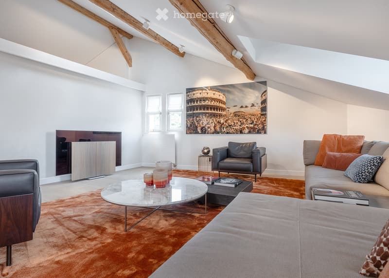 Modern living room with exposed wooden beams, large windows, a fireplace, a sofa, armchair, coffee table, and artwork on the wall.