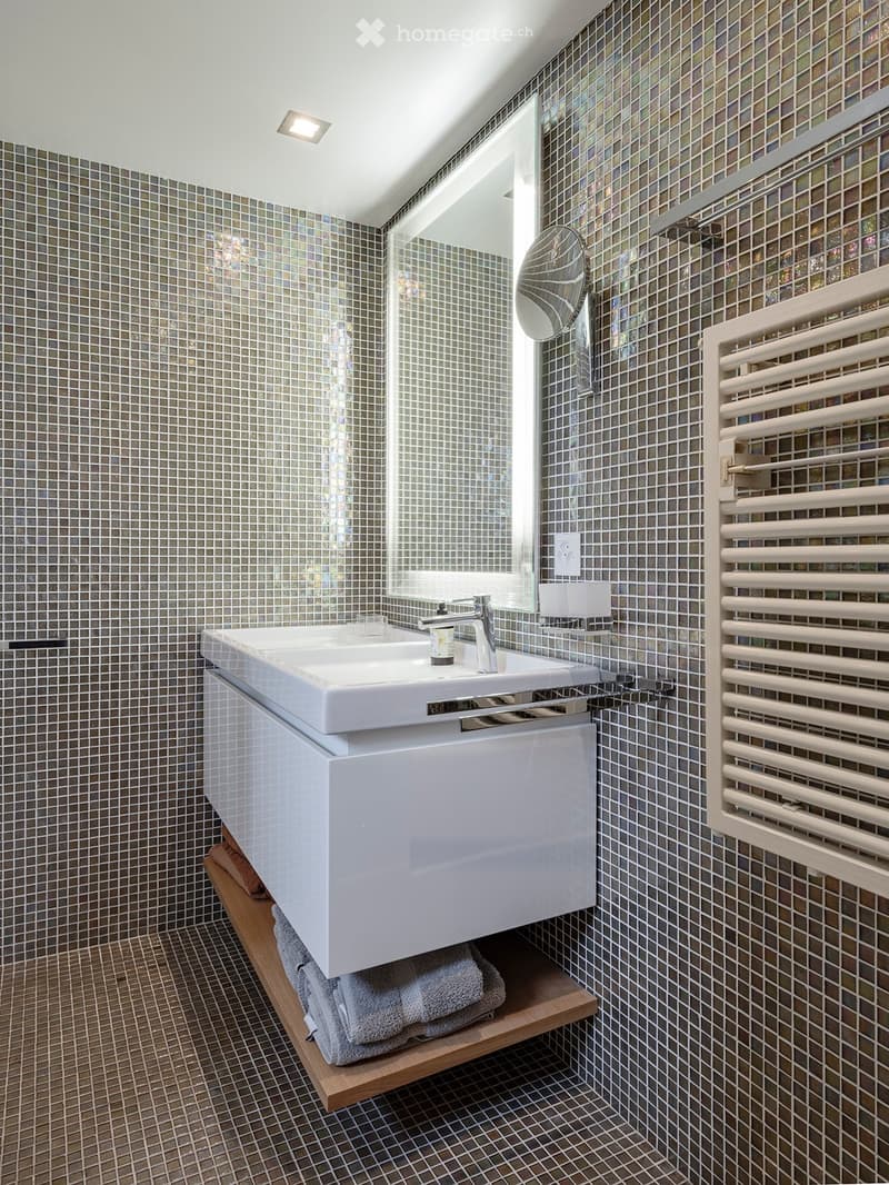 Modern bathroom with a white sink, chrome faucet, large mirror, towel rack, and neatly folded towels on a wooden shelf.