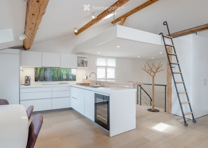 Modern kitchen with white cabinets, a central island, and a wooden floor. Features include a sink, oven, coffee maker, and a ladder leading to an upper level.