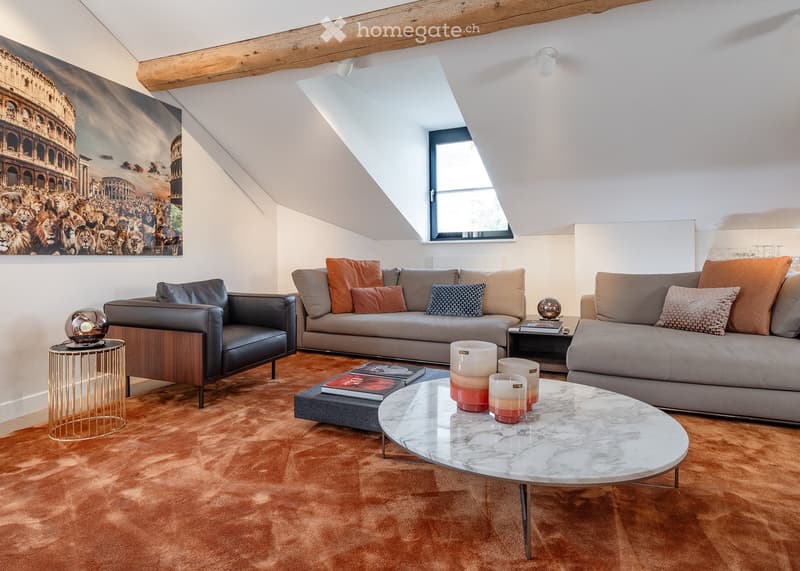 Modern living room with exposed wooden beams, large window, beige sofa, leather armchair, marble coffee table, side table, books, candles, and decorative spheres.