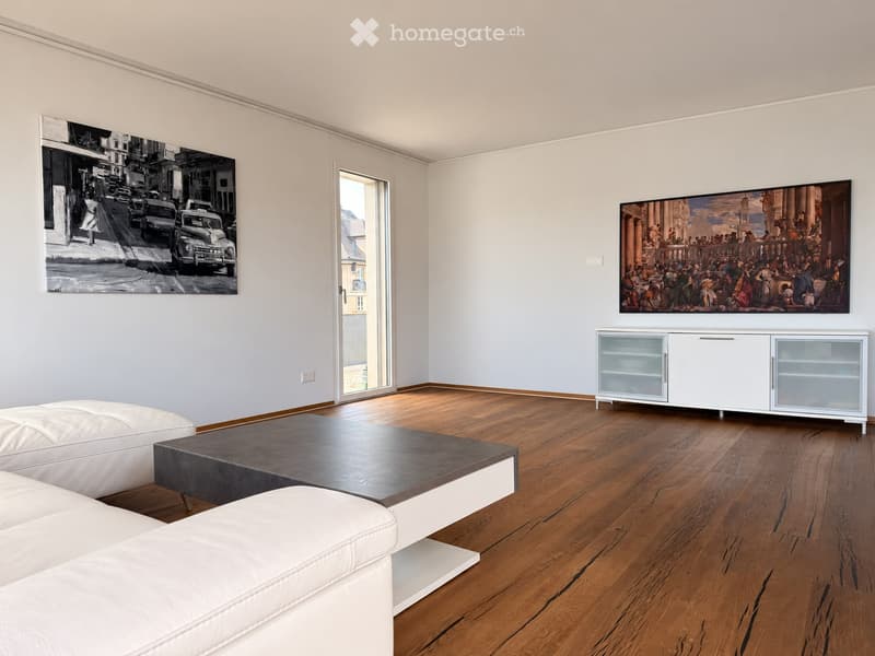 Modern living room with light grey walls, wooden flooring, white leather sofa, dark coffee table, and a white cabinet with glass doors.
