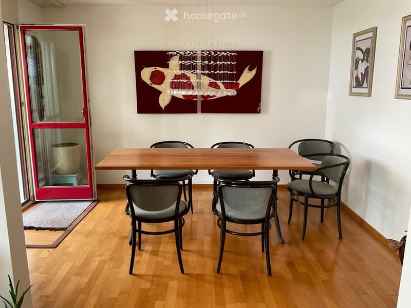 Dining area with a wooden table and six chairs, light wooden flooring, and artwork on the walls.