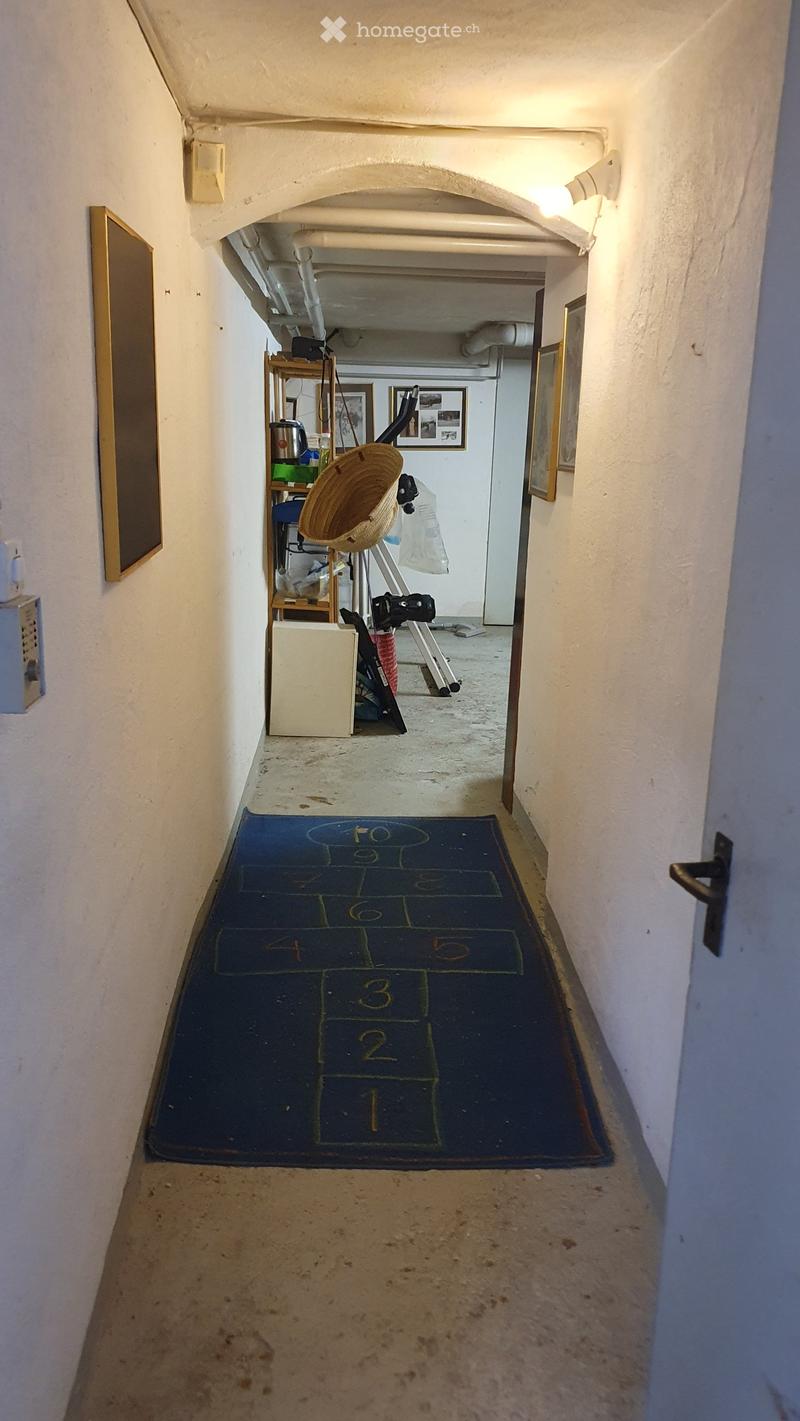 A narrow hallway with white walls, a blue numbered mat on the floor, and a small shelf with items in the background.