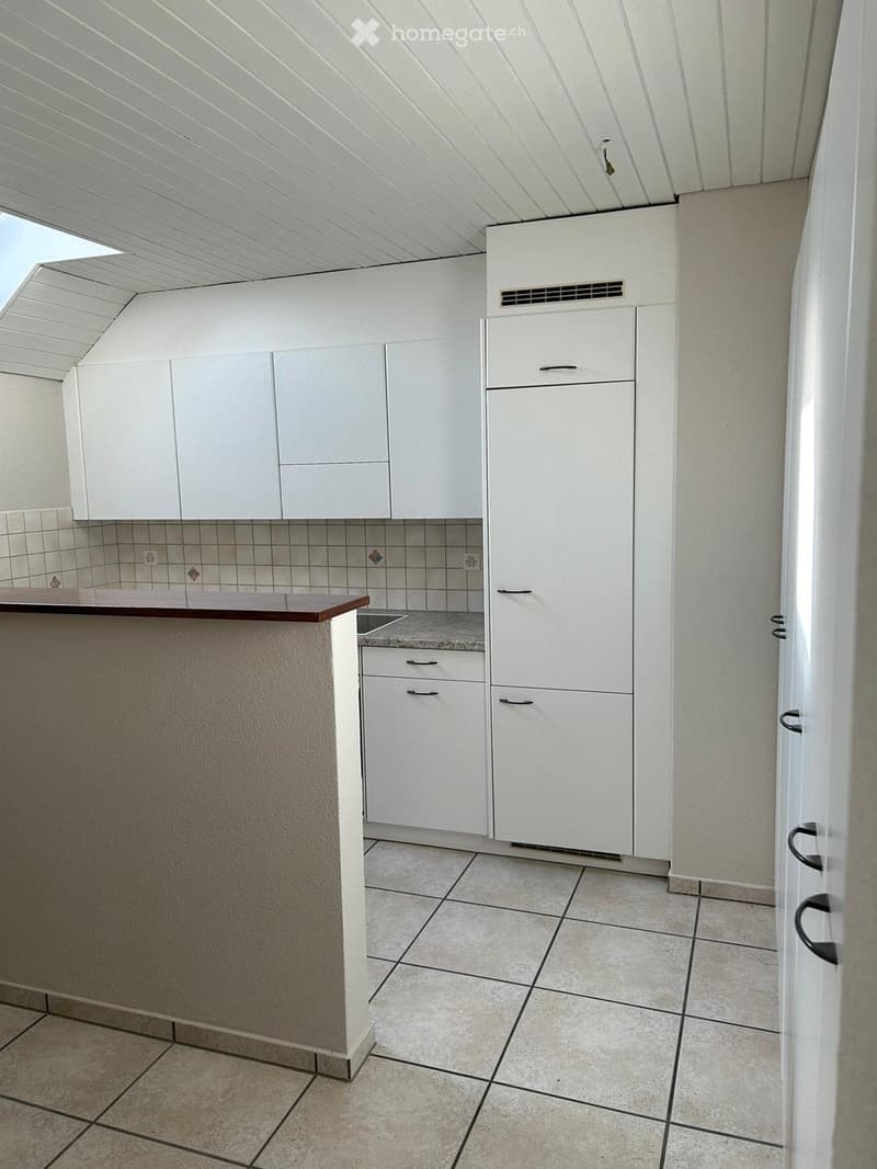 Modern kitchen with white cabinets, a refrigerator, and a countertop, featuring tiled flooring and a slanted ceiling.
