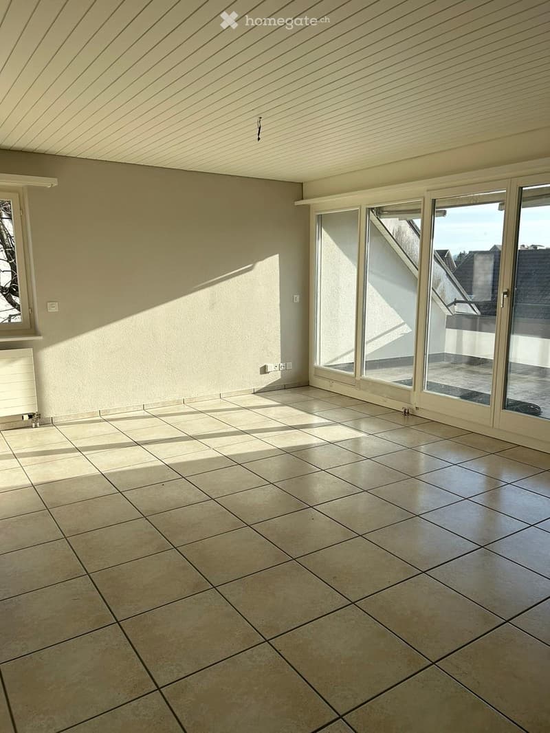 Empty room with tiled floor, large windows, and a slanted ceiling. No furniture or equipment present.