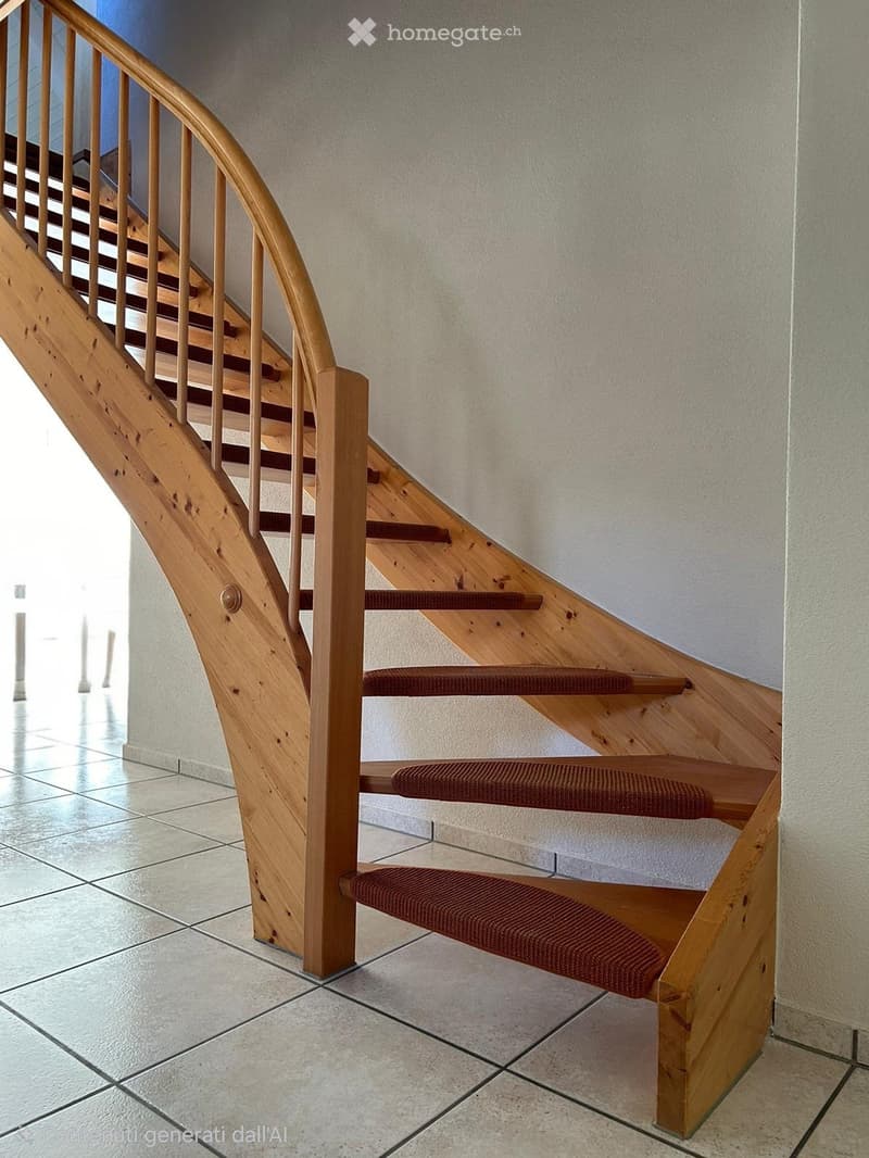 Wooden staircase with red carpeted steps and a wooden handrail, leading upwards in a well-lit interior space with tiled flooring and light-colored walls.