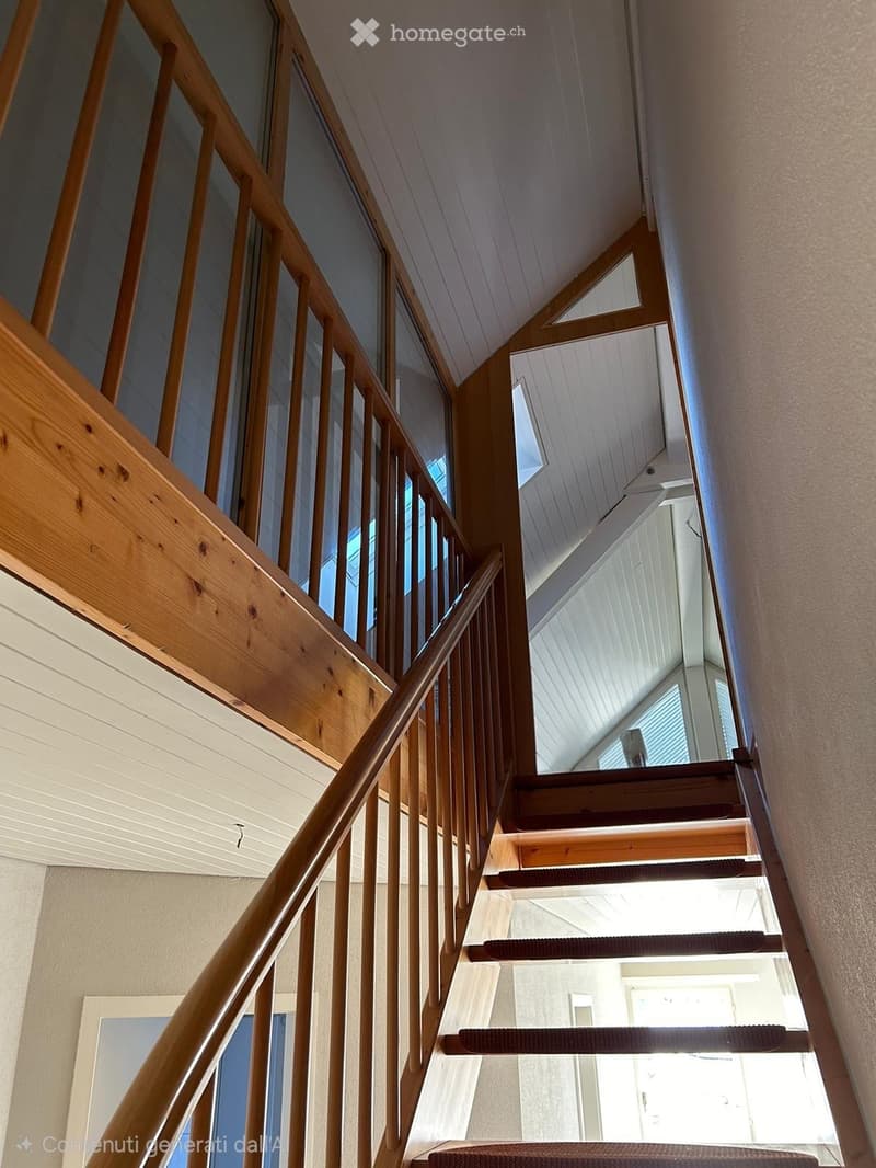 Wooden staircase with a handrail and carpeted steps, leading to an upper level with a slanted ceiling and skylight windows.
