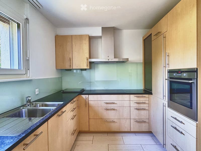 Modern kitchen with light wooden cabinets, stainless steel appliances, and a dark countertop.