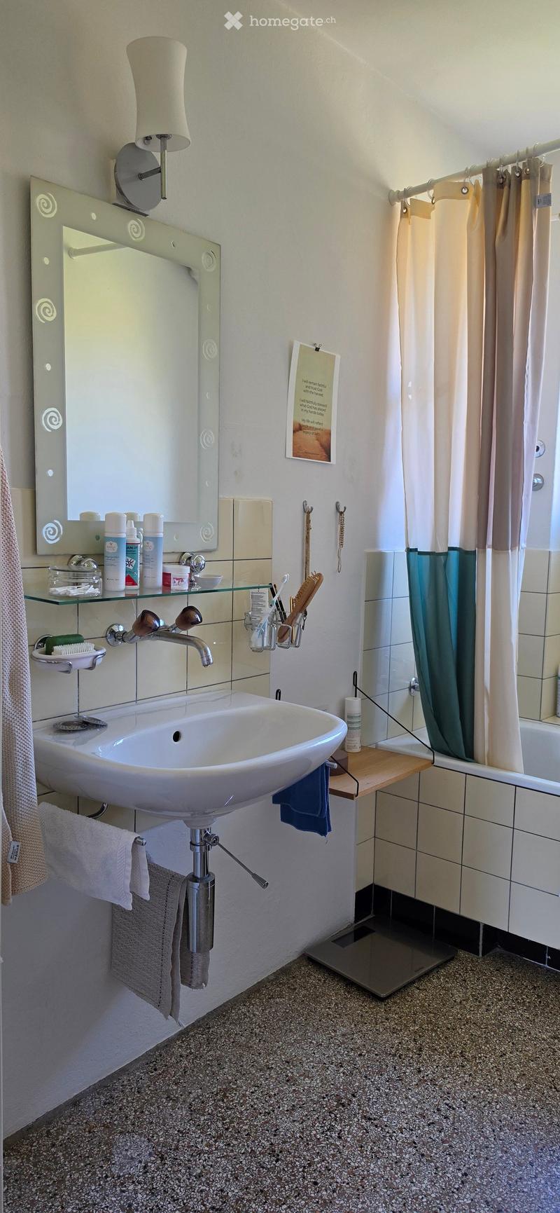 Modern bathroom with a white sink, glass shelf, mirror, and shower area with a curtain. Includes towels, toiletries, and a scale on the floor.