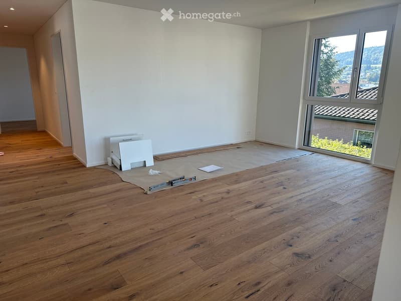 Empty room with wooden flooring, white walls, and large windows offering a view of the outdoors.
