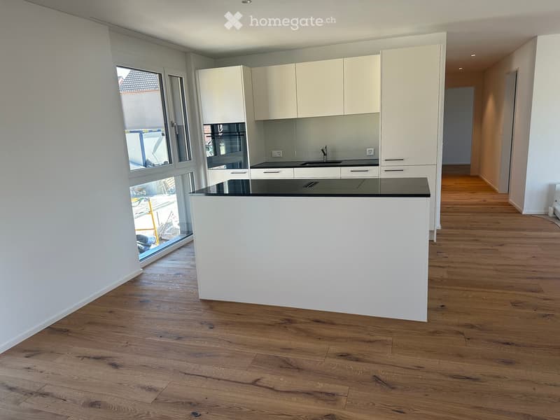 Modern kitchen with white cabinets, a central island, and a black countertop. The space features wooden flooring and large windows offering a view outside.