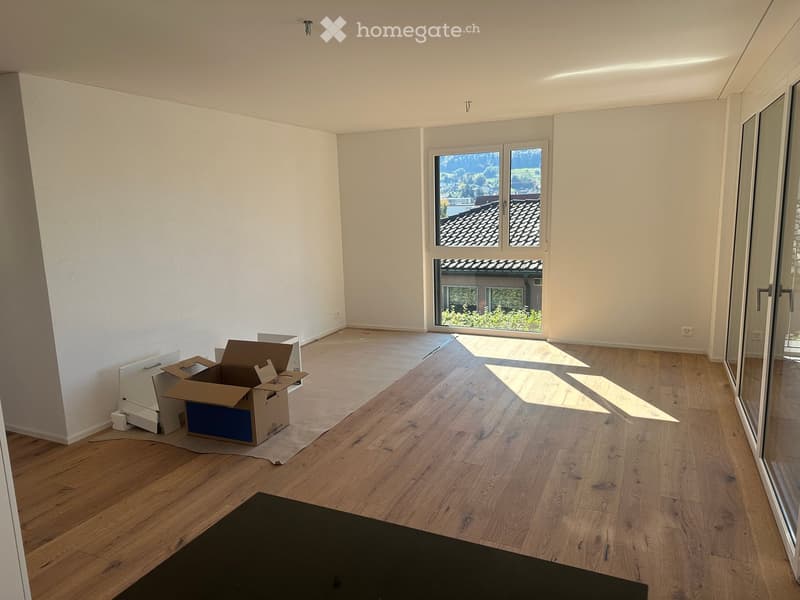Empty room with wooden flooring, white walls, large windows, and a sliding glass door leading to a balcony.