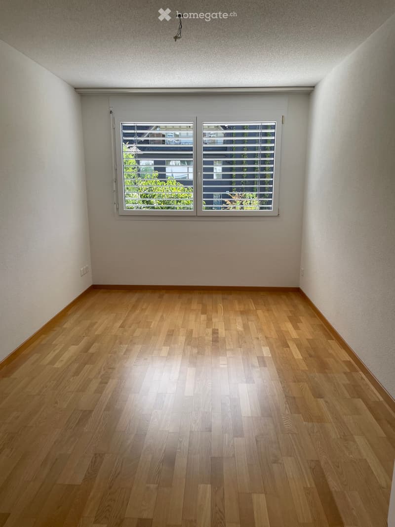 Empty room with wooden flooring, white walls, and large windows with blinds. No furniture or equipment present.