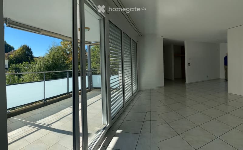 Modern balcony with large glass sliding doors, tiled floor, metal railing, and a view of greenery outside.