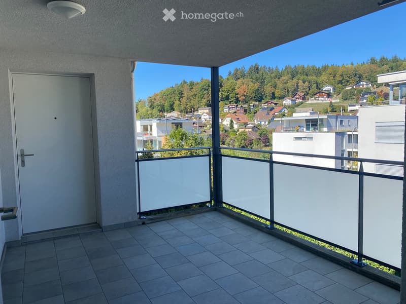 Balcony with tiled floor, white railing, and a door leading inside. Offers a scenic view of a residential area with houses and trees.