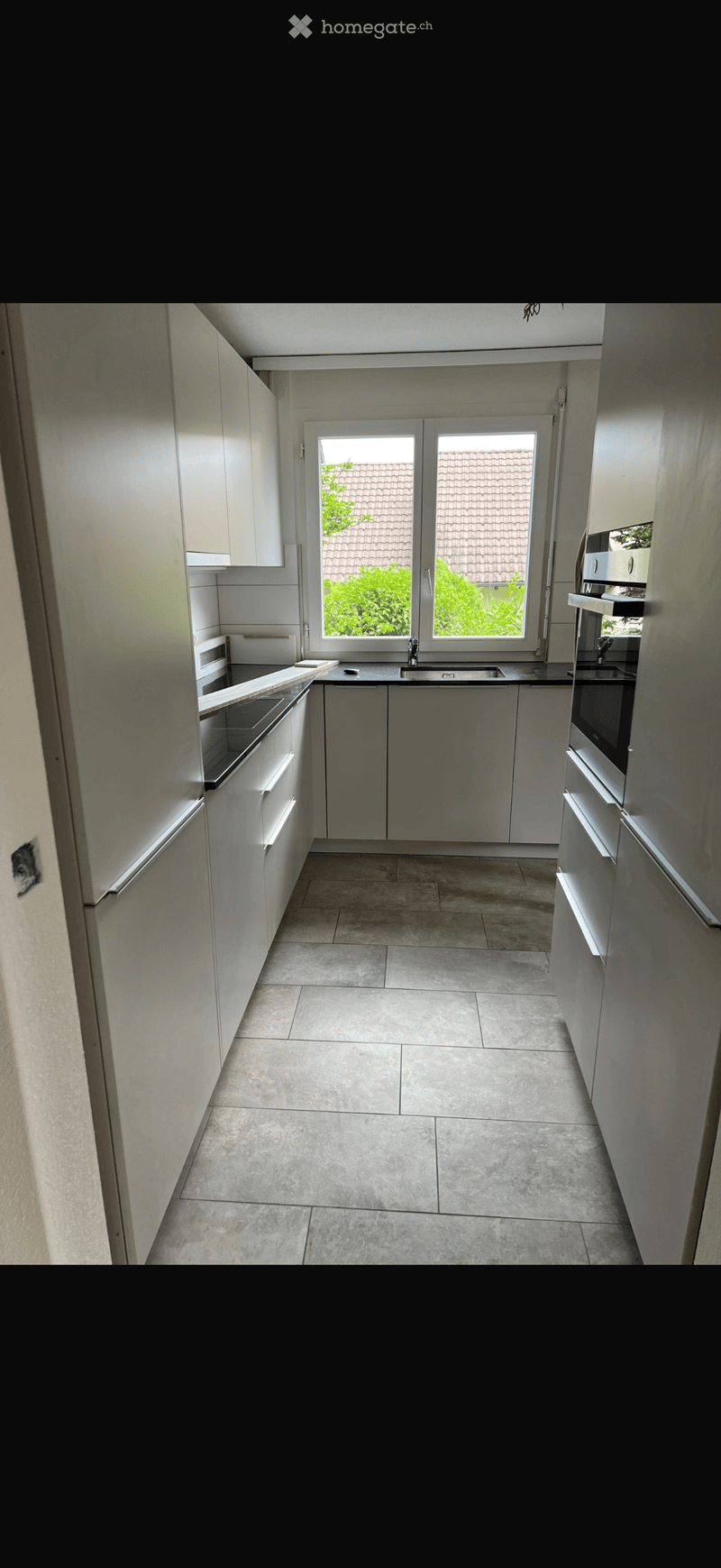 Modern kitchen with white cabinets, stainless steel appliances, and a large window overlooking a garden.