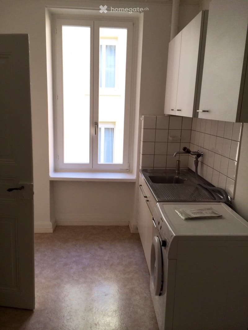 Small kitchen, tiled wall, white cabinets, sink, washing machine, window with ledge
