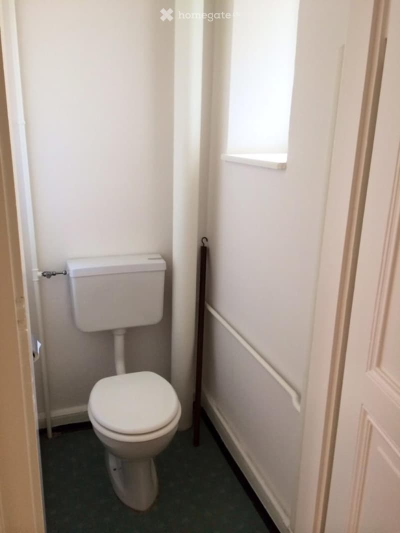 A small bathroom with a white toilet, a small window and a towel hanger.
