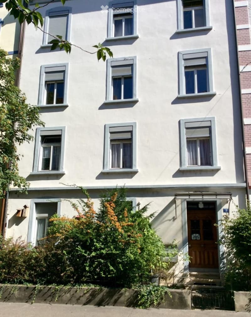 White building, multiple windows, wooden door, small plants in front