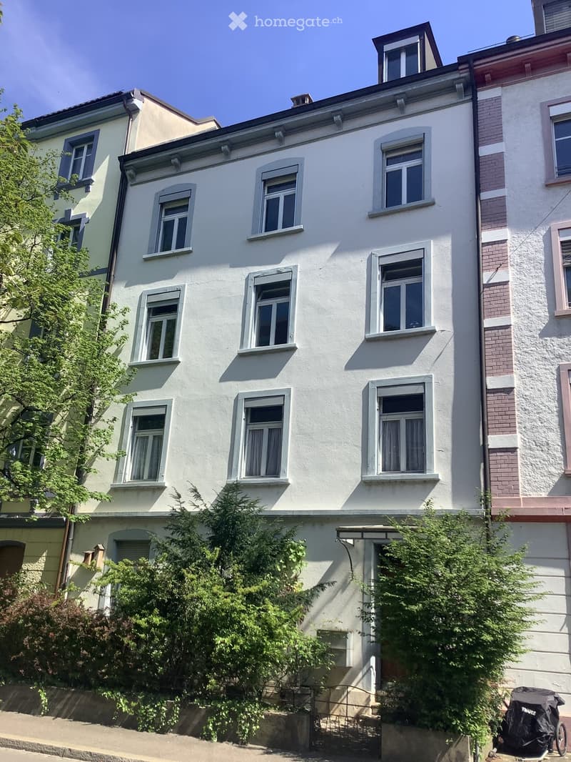 white-painted residential building with multiple windows, beige bricks on lower floor, metal railings on ground floor