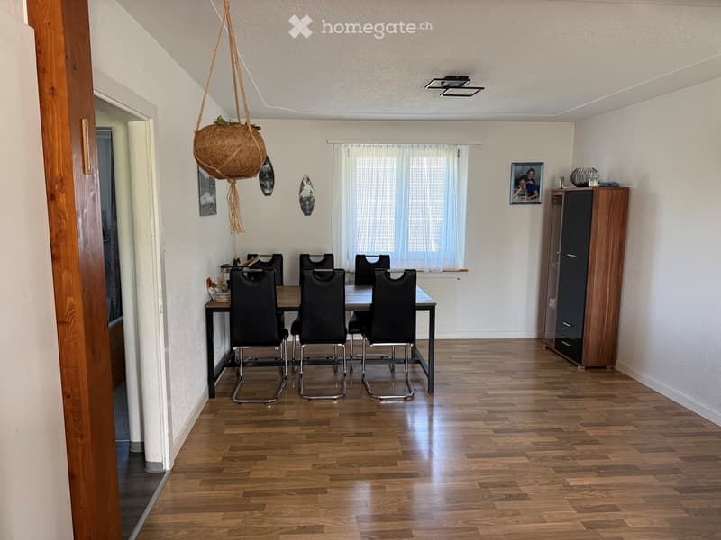 Dining room with wooden flooring, a dining table surrounded by black chairs, a wooden cabinet, and a hanging basket with a plant.