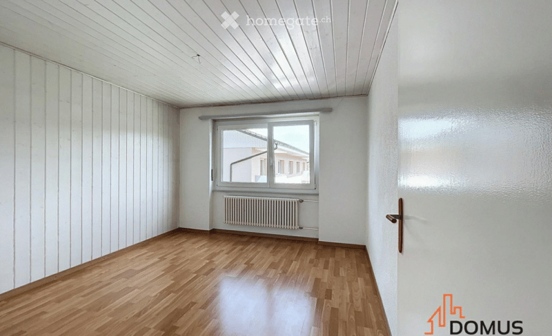 Empty room with wooden flooring, white walls, and a window with a radiator below it.