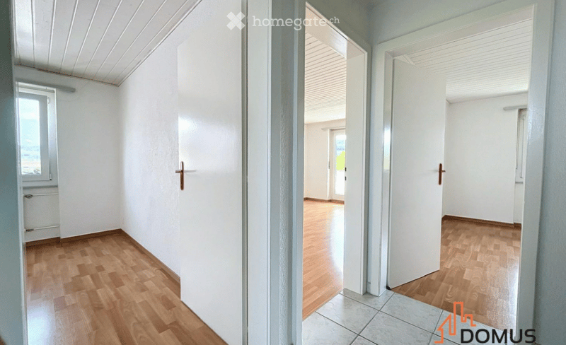 Empty hallway with wooden flooring, white walls, and multiple doors leading to other rooms.