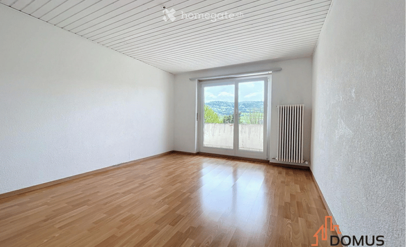 Empty room with wooden flooring, white walls, and a large sliding glass door leading to a balcony with a scenic view.